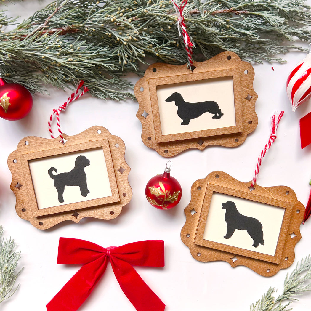 Wooden frames with dog silhouettes, red ribbon, and Christmas ornaments on a white background