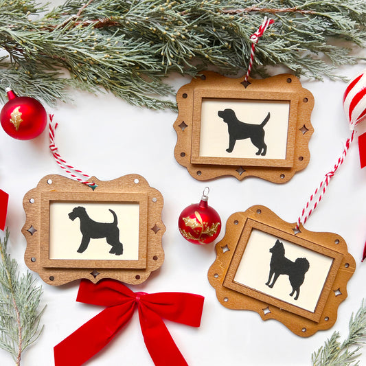 Wooden frames with dog silhouettes, red ribbon, and Christmas ornaments on a white background.