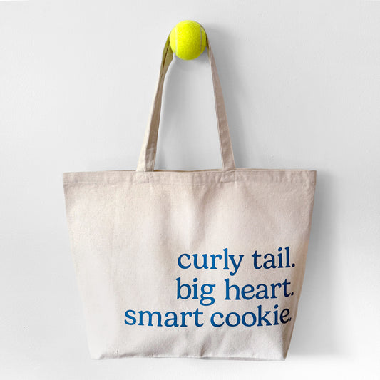 Tote bag with text 'curly tail. big heart. smart cookie' on a white background