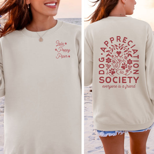 Beige sweatshirt with 'Dog Appreciation Society' text and floral design on a beach.