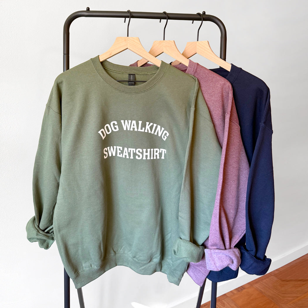 Green sweatshirt with 'Dog Walking Sweatshirt' text on a rack with other sweatshirts.