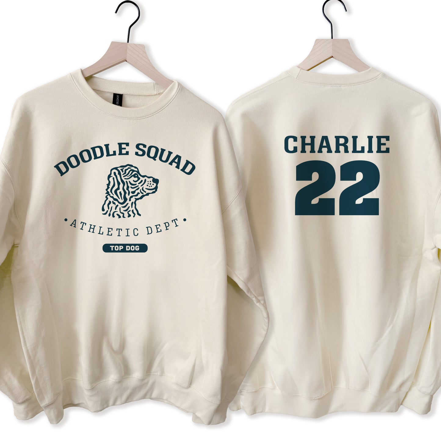 Beige sweatshirt with 'Doodle Squad Athletic Dept' on the front and 'CHARLIE 22' on the back, displayed on hangers.