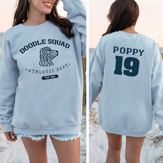 Light blue sweatshirt with 'Doodle Squad' and 'Poppy 19' text on a beach.