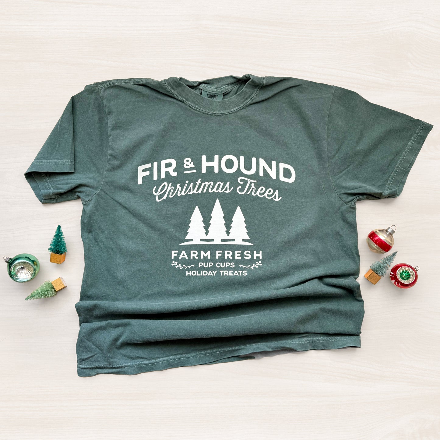 Green t-shirt with 'Fir & Hound Christmas Trees' text and graphics on a light background