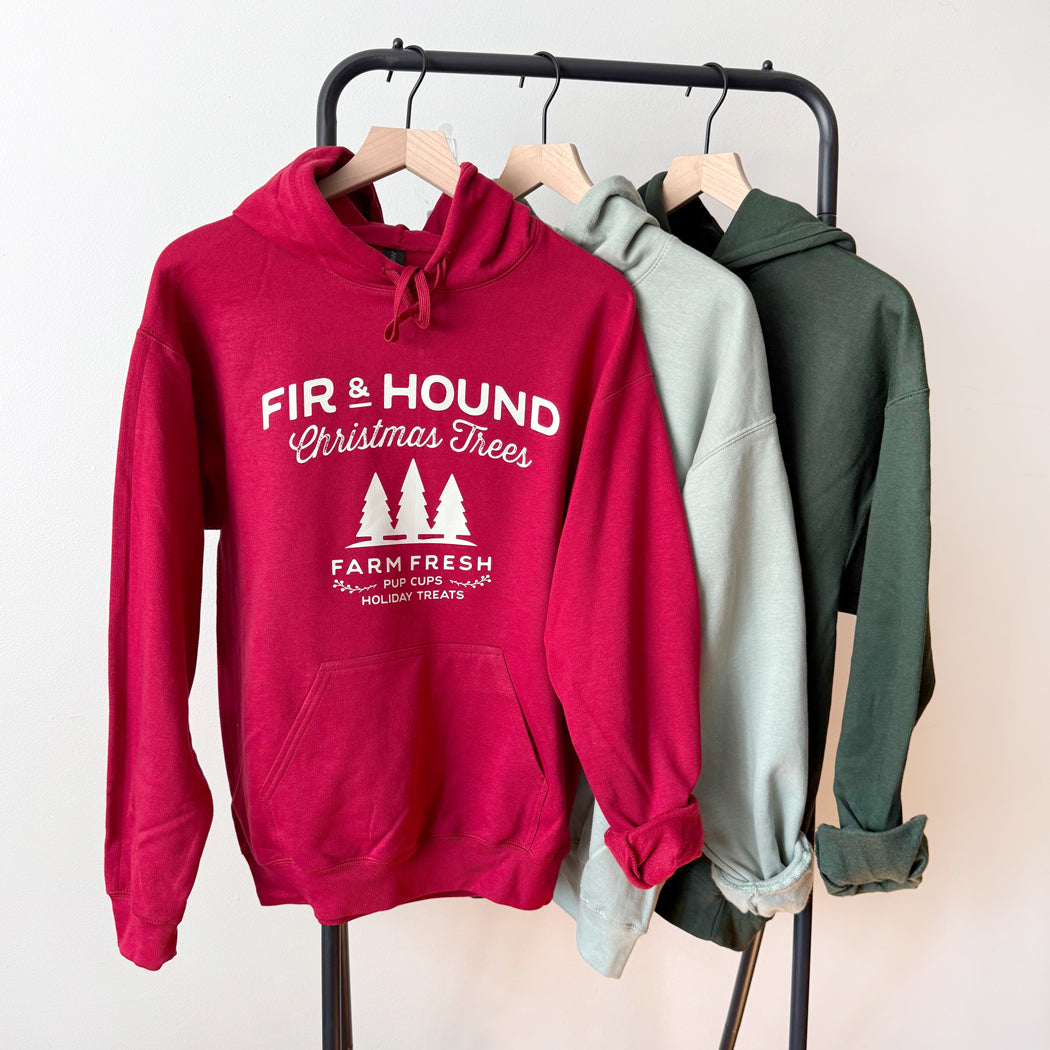 Red hoodie with 'Fir & Hound' text and graphics on a rack with other hoodies.