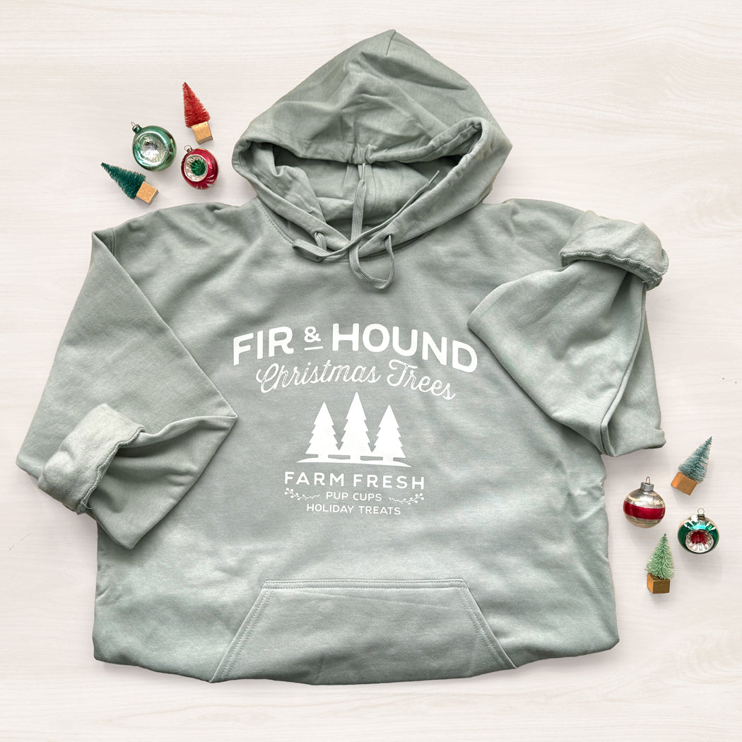 Light green hoodie with 'Fir & Hound Christmas Trees' text and graphics on a light background with Christmas ornaments.