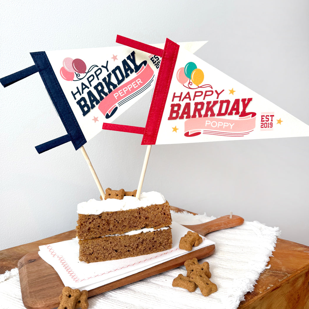 Dog birthday cake with 'Happy Barkday' flags on a wooden board.
