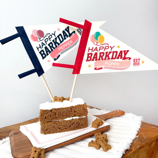 Dog birthday cake with 'Happy Barkday' flags on a wooden board.
