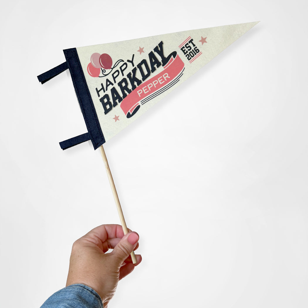 Hand holding a small flag with 'Happy Barkday Pepper' text on a white background