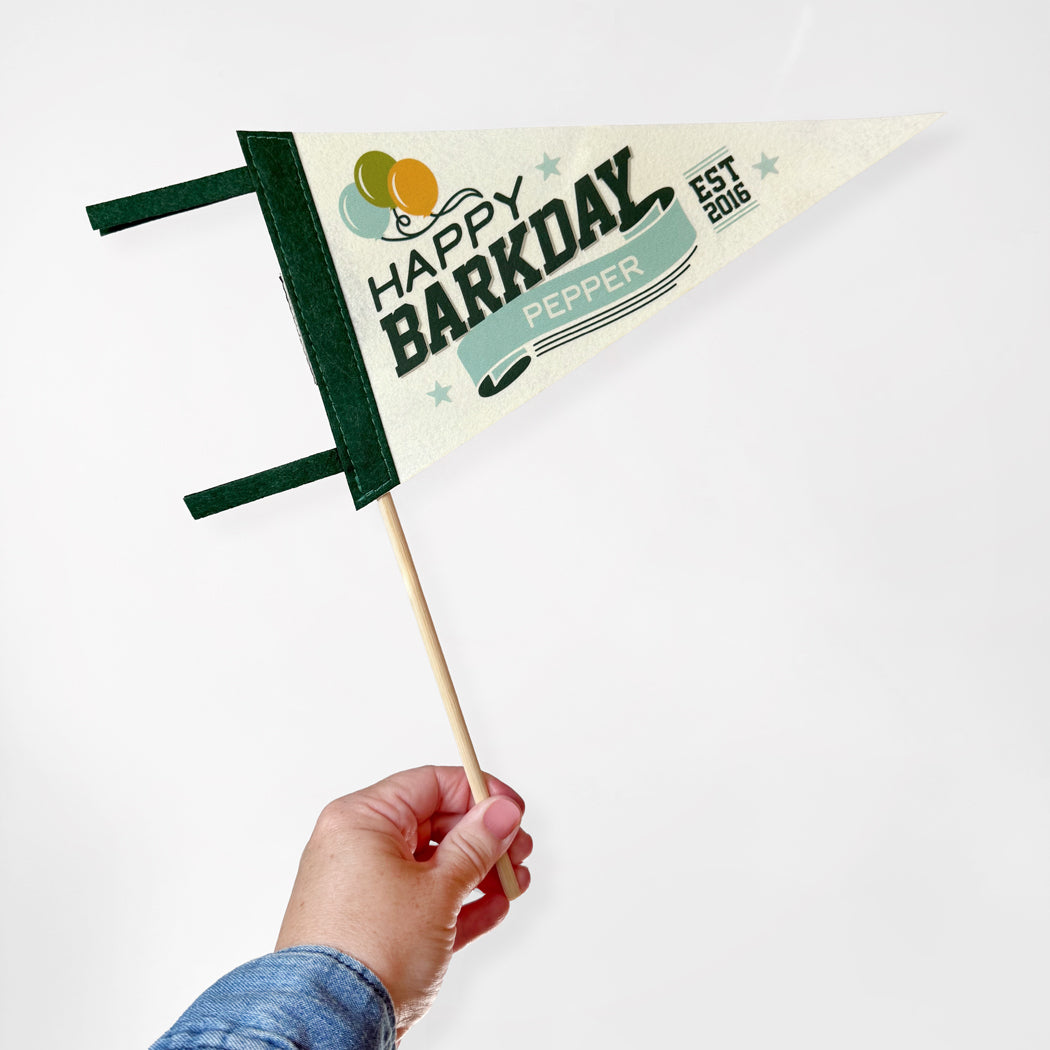Hand holding a small flag with 'Happy Barkday Pepper' text on a white background