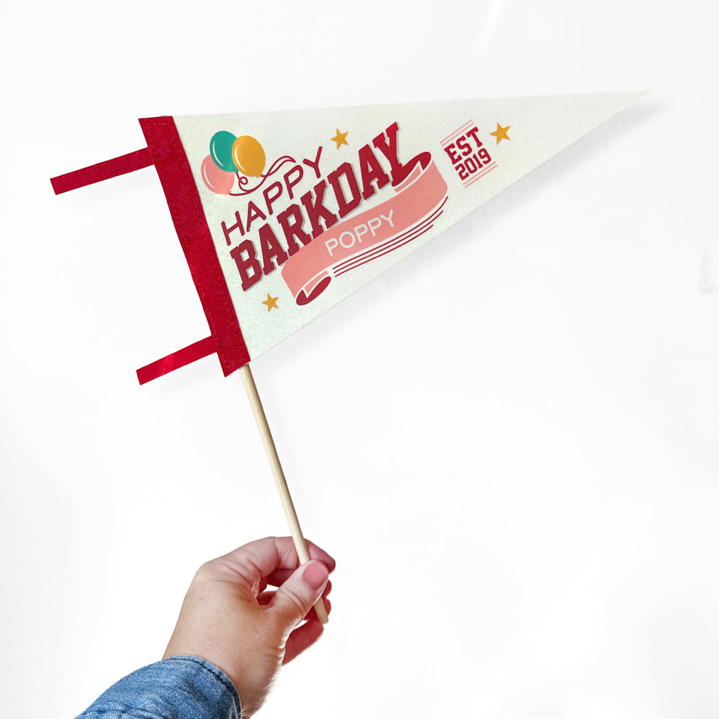 Hand holding a small flag with 'Happy Barkday Poppy' text on a white background