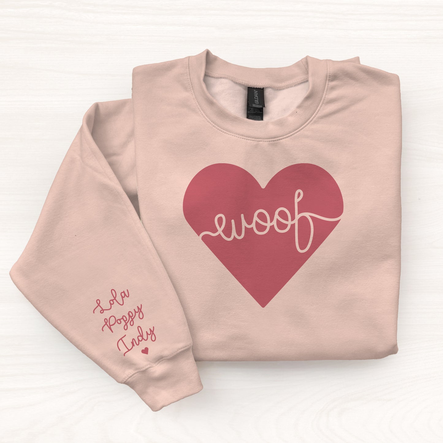 Folded pink sweatshirt with a red heart and 'woof' text on a white background