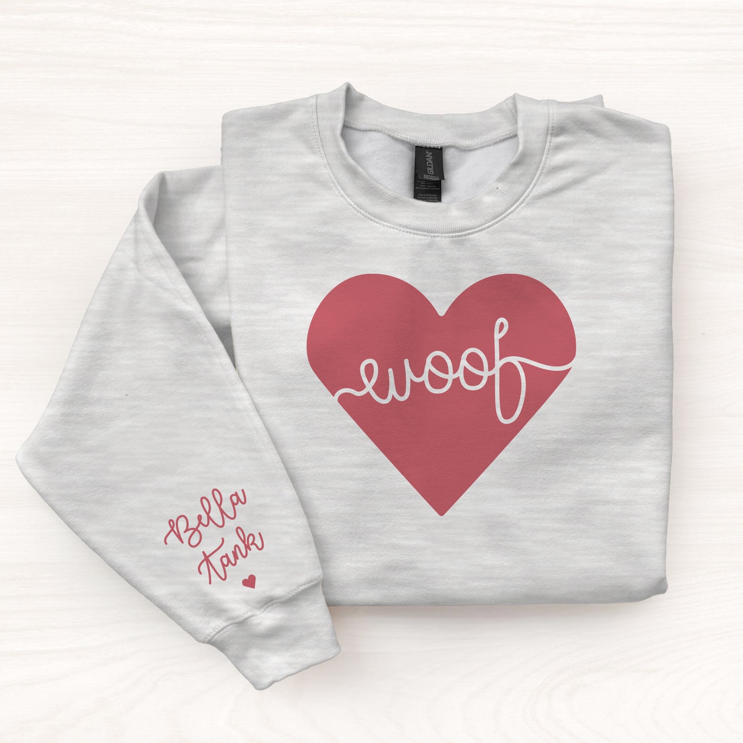Folded gray sweatshirt with a red heart and 'woof' text on a white background