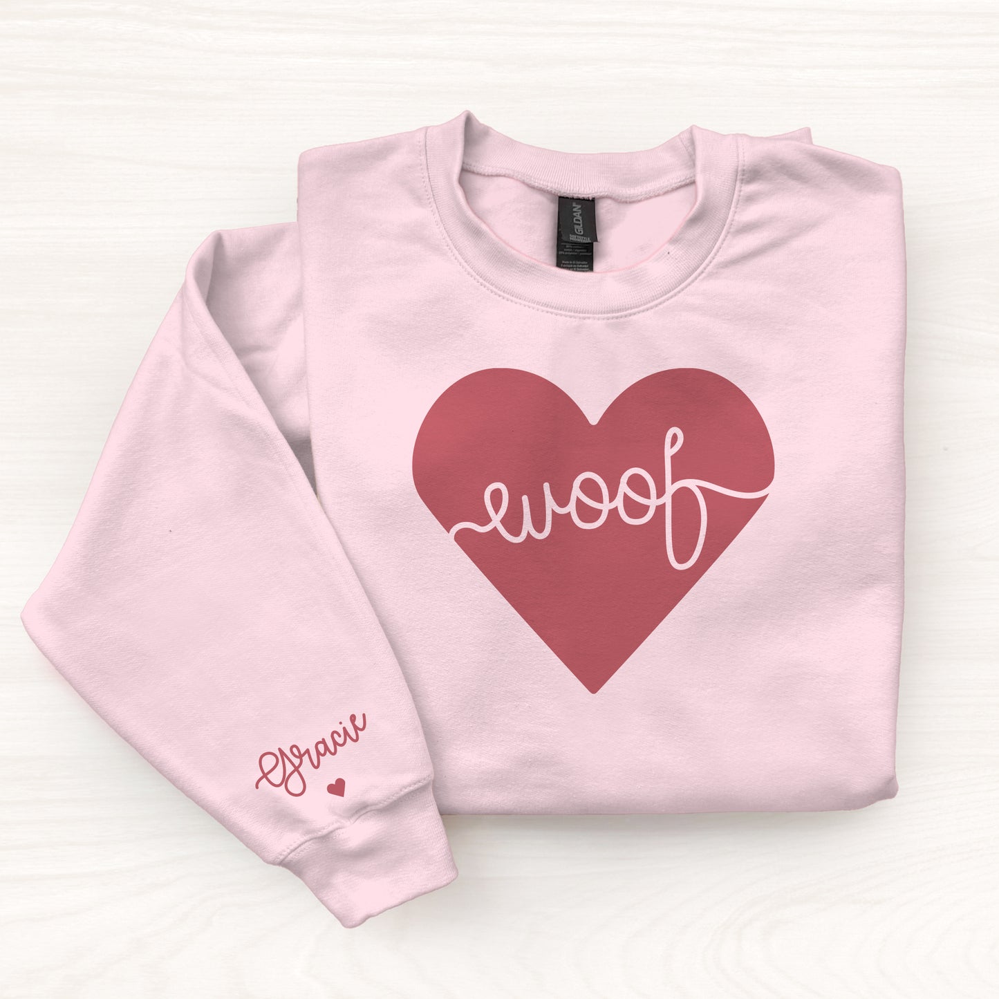Pink sweatshirt with a red heart and 'woof' text on a white background