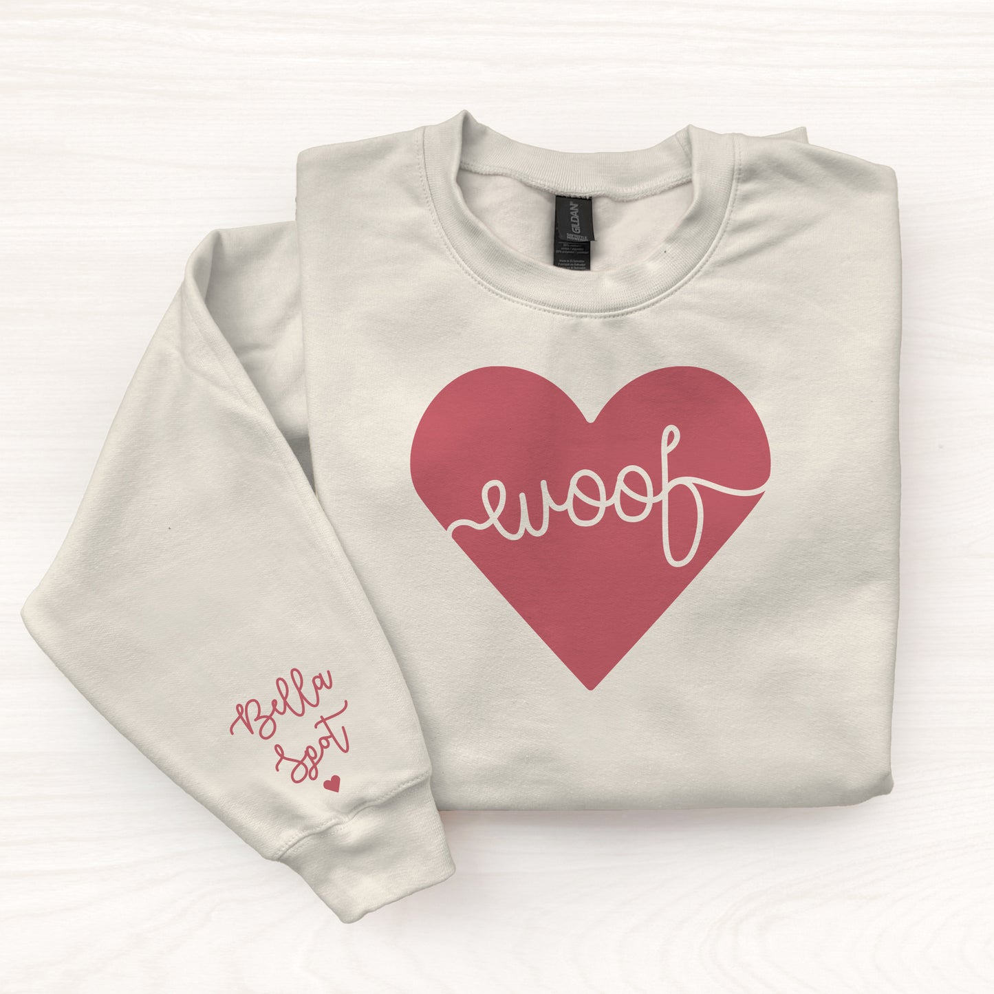 Folded beige sweatshirt with a red heart and 'woof' text on a white background