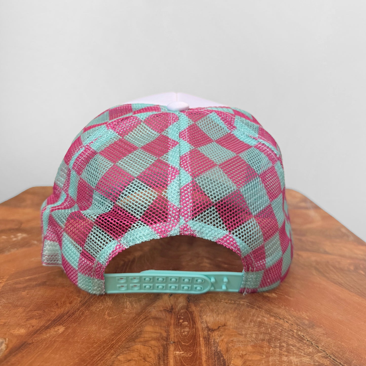 Checkered pink and green cap on a wooden surface with a white background
