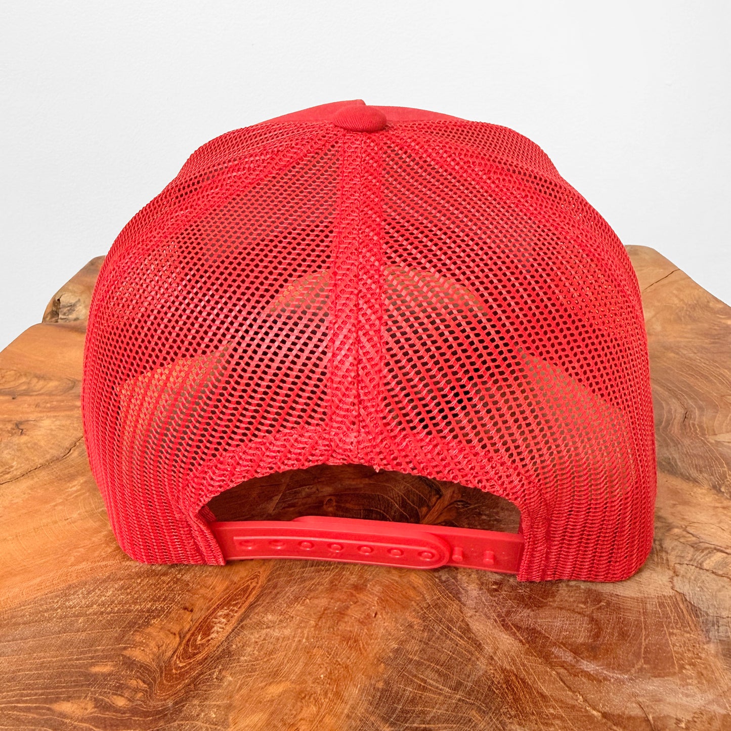 Red mesh cap on a wooden surface with a white background