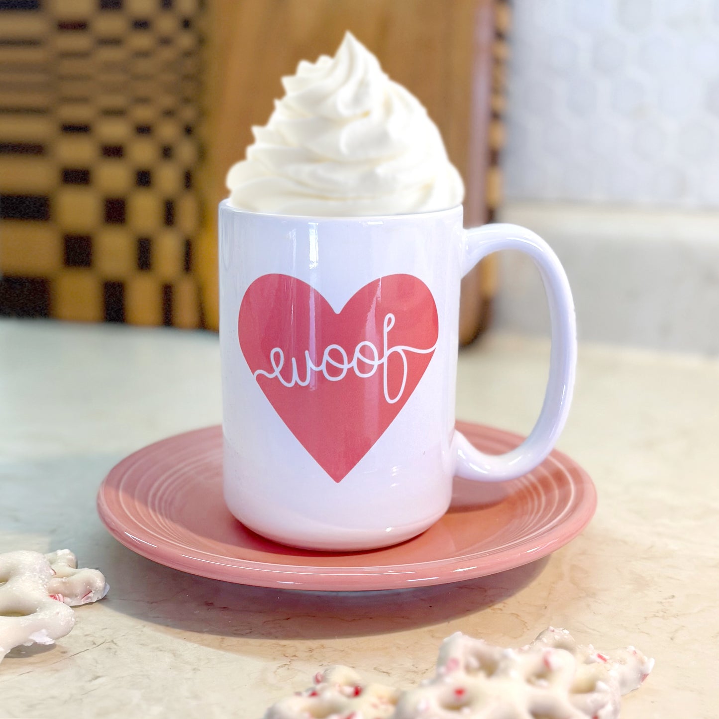 White mug with pink heart and 'woof' text on a pink saucer, filled with hot chocolate and whipped cream.