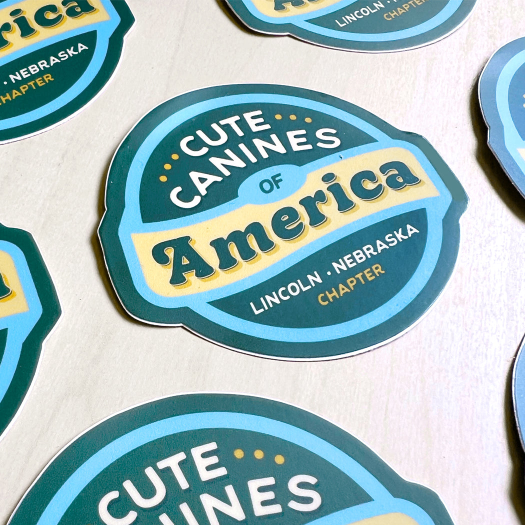 Cute Canines of America – Lincoln, Nebraska sticker featuring a blue, teal, and yellow design.