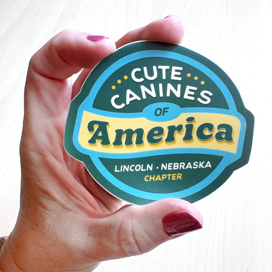 Cute Canines of America – Lincoln, Nebraska sticker featuring a blue, teal, and yellow design.
