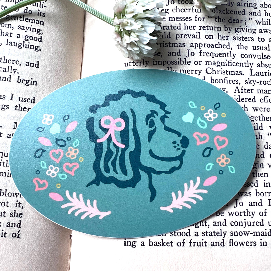 Oval sticker featuring a doodle dog with pink and blue hearts, flowers, and leaves.