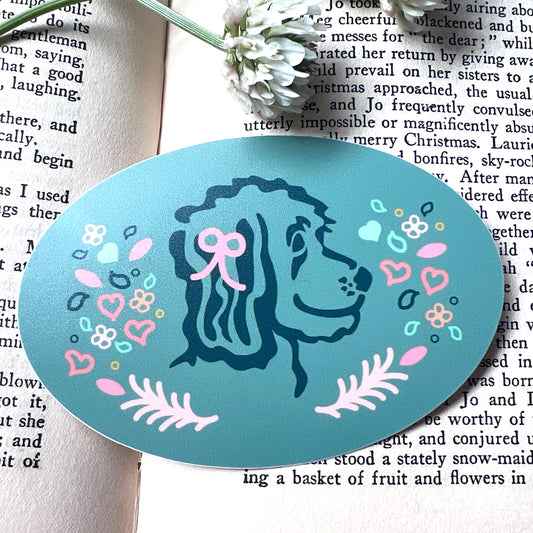Oval sticker featuring a doodle dog with pink and blue hearts, flowers, and leaves.