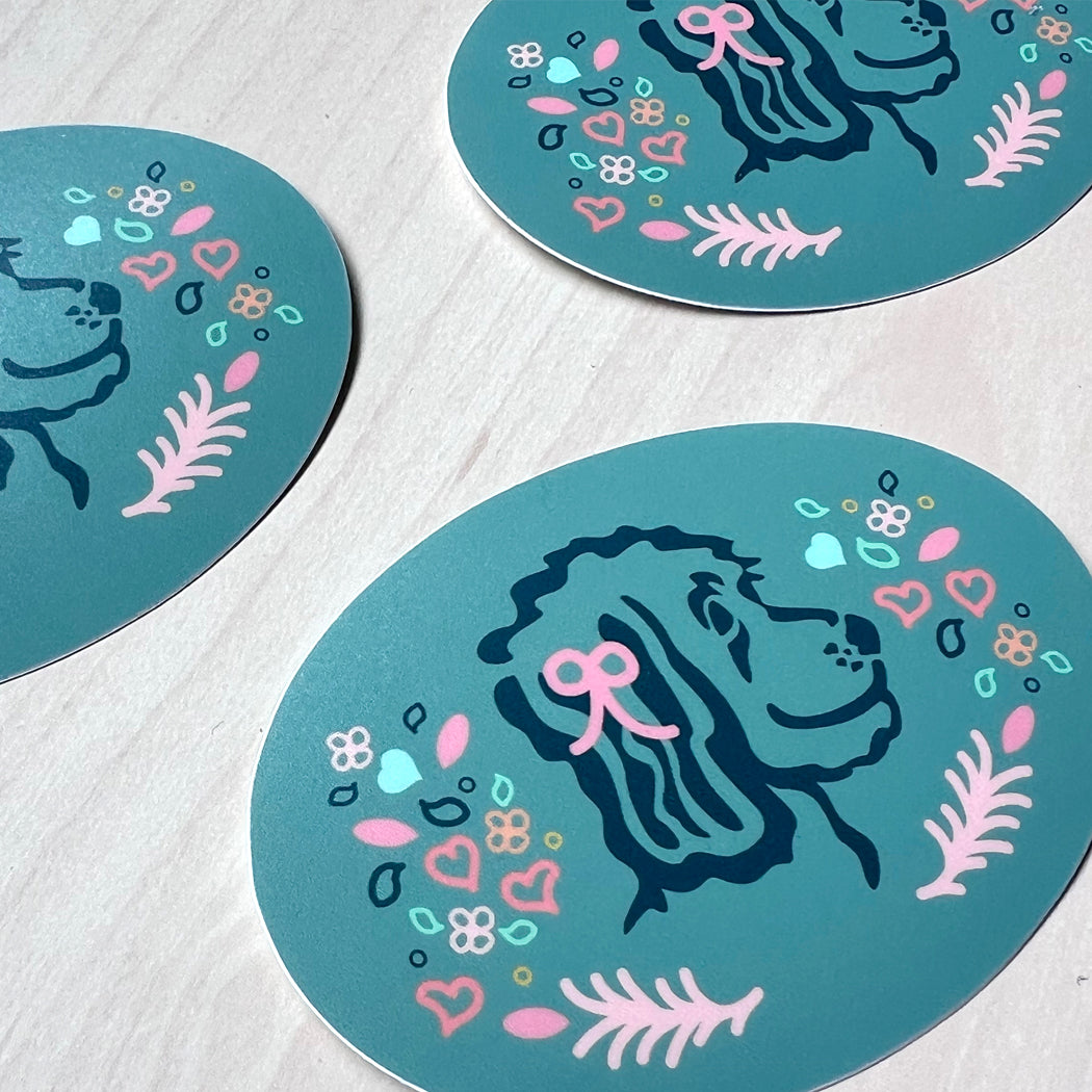 Oval sticker featuring a doodle dog with pink and blue hearts, flowers, and leaves.
