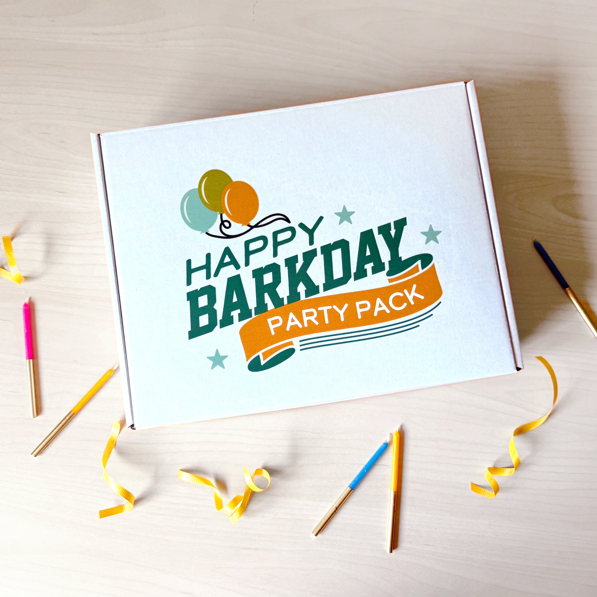 Box labeled 'Happy Barkday Party Pack' on a wooden surface with party supplies.