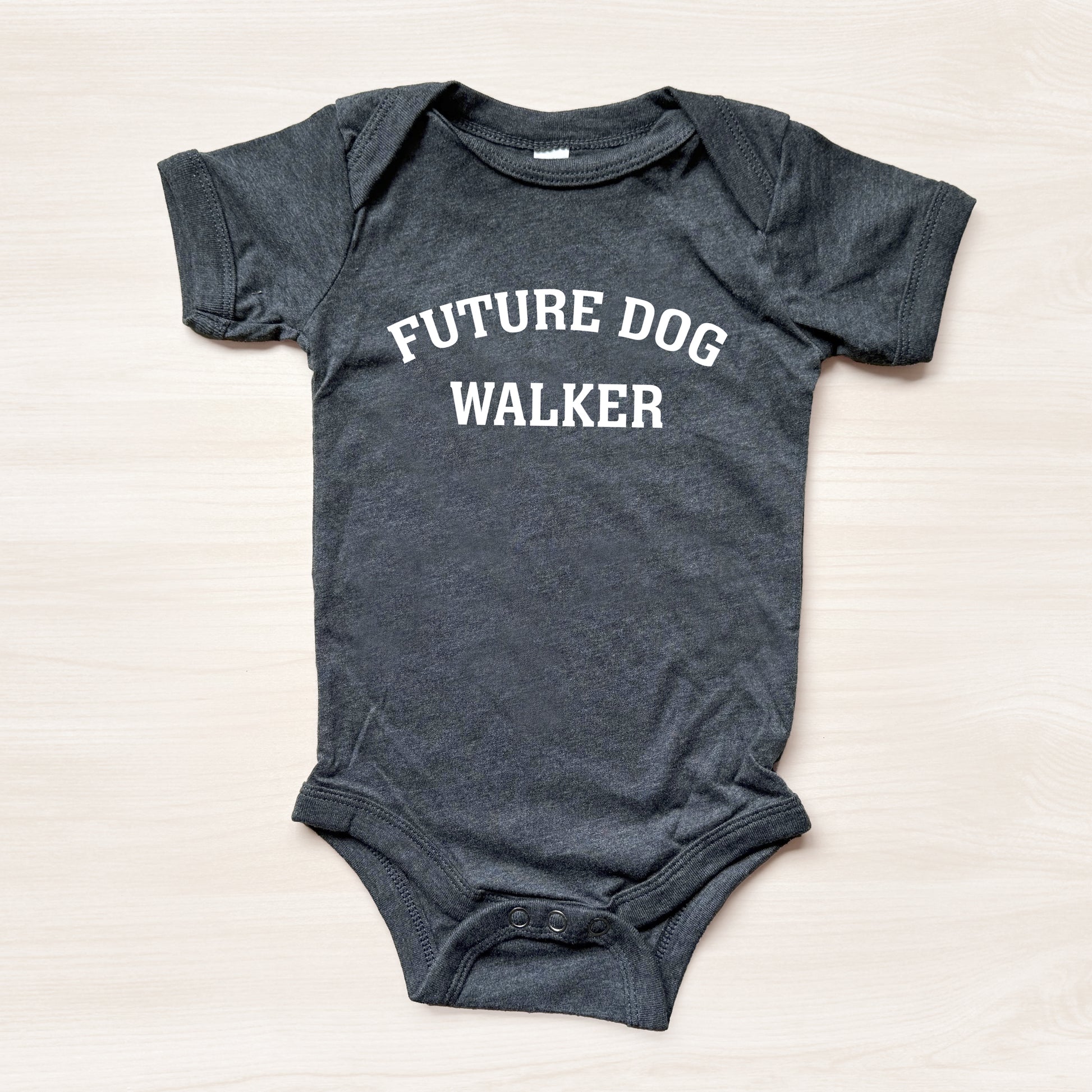 Gray baby onesie with 'Future Dog Walker' text on a light beige background