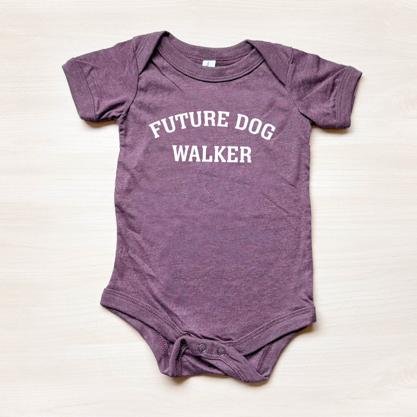 Purple baby onesie with 'Future Dog Walker' text on a beige background