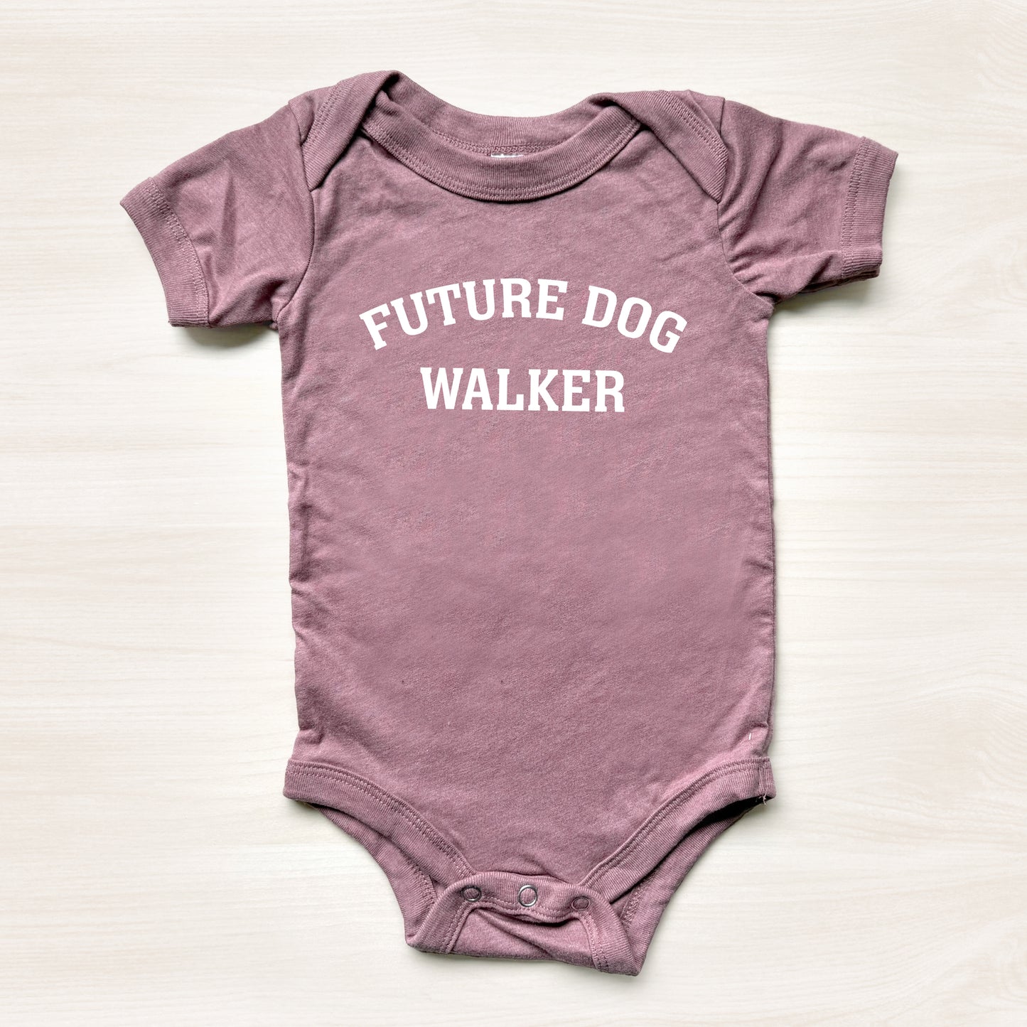 Mauve baby onesie with 'Future Dog Walker' text on a light background