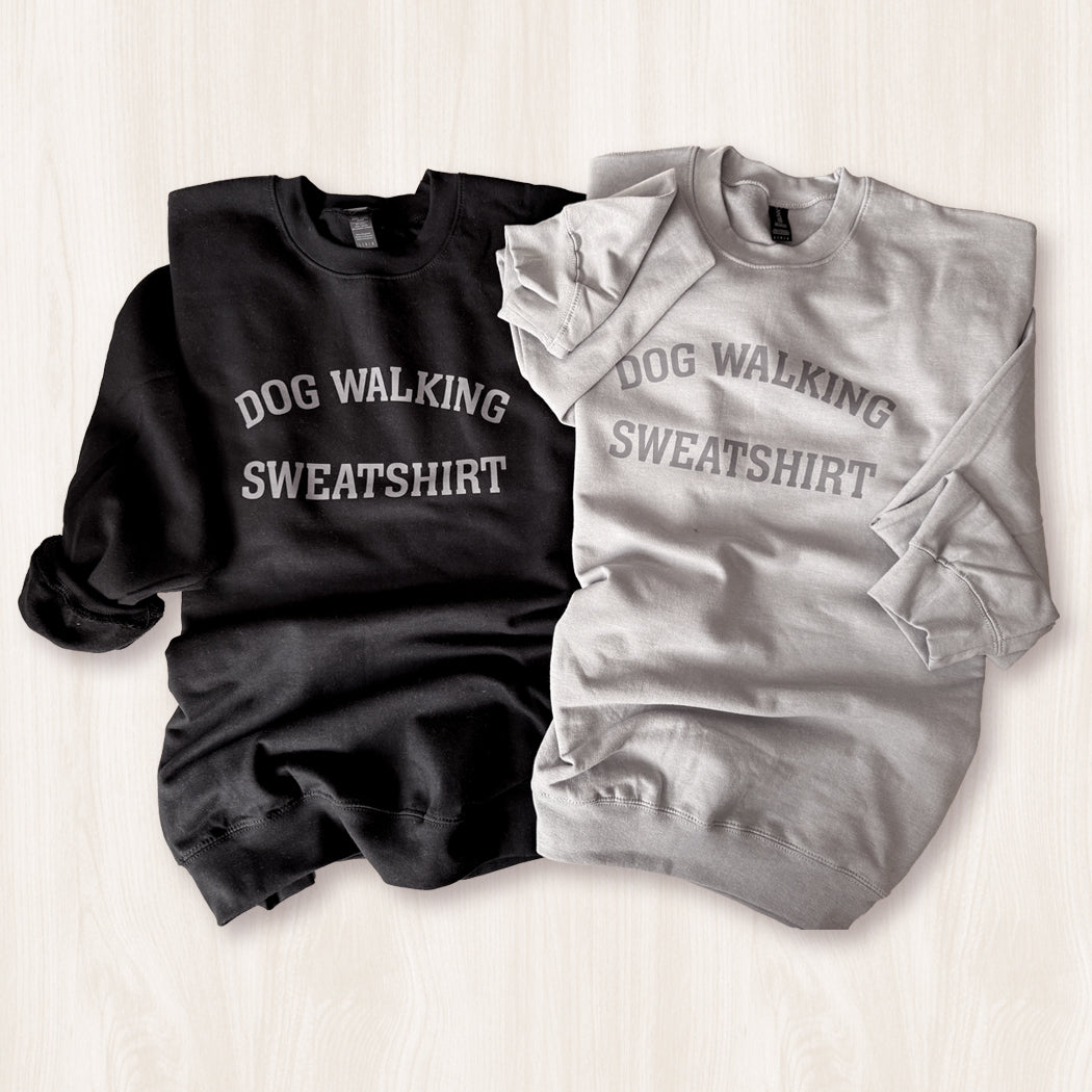 Black and gray sweatshirts with 'DOG WALKING SWEATSHIRT' text on a light wooden surface.