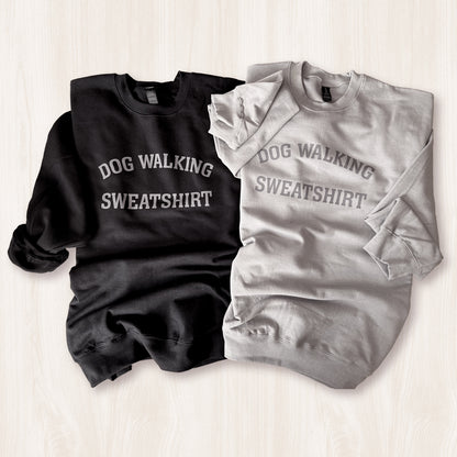 Black and gray sweatshirts with 'DOG WALKING SWEATSHIRT' text on a light wooden surface.
