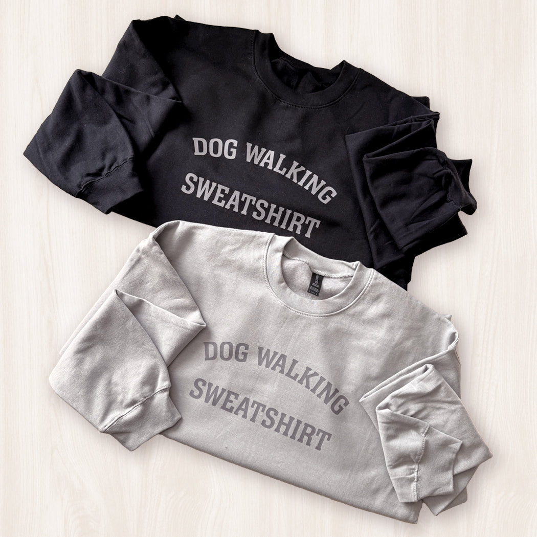 Black and gray sweatshirts with 'DOG WALKING SWEATSHIRT' text on a light wooden surface.