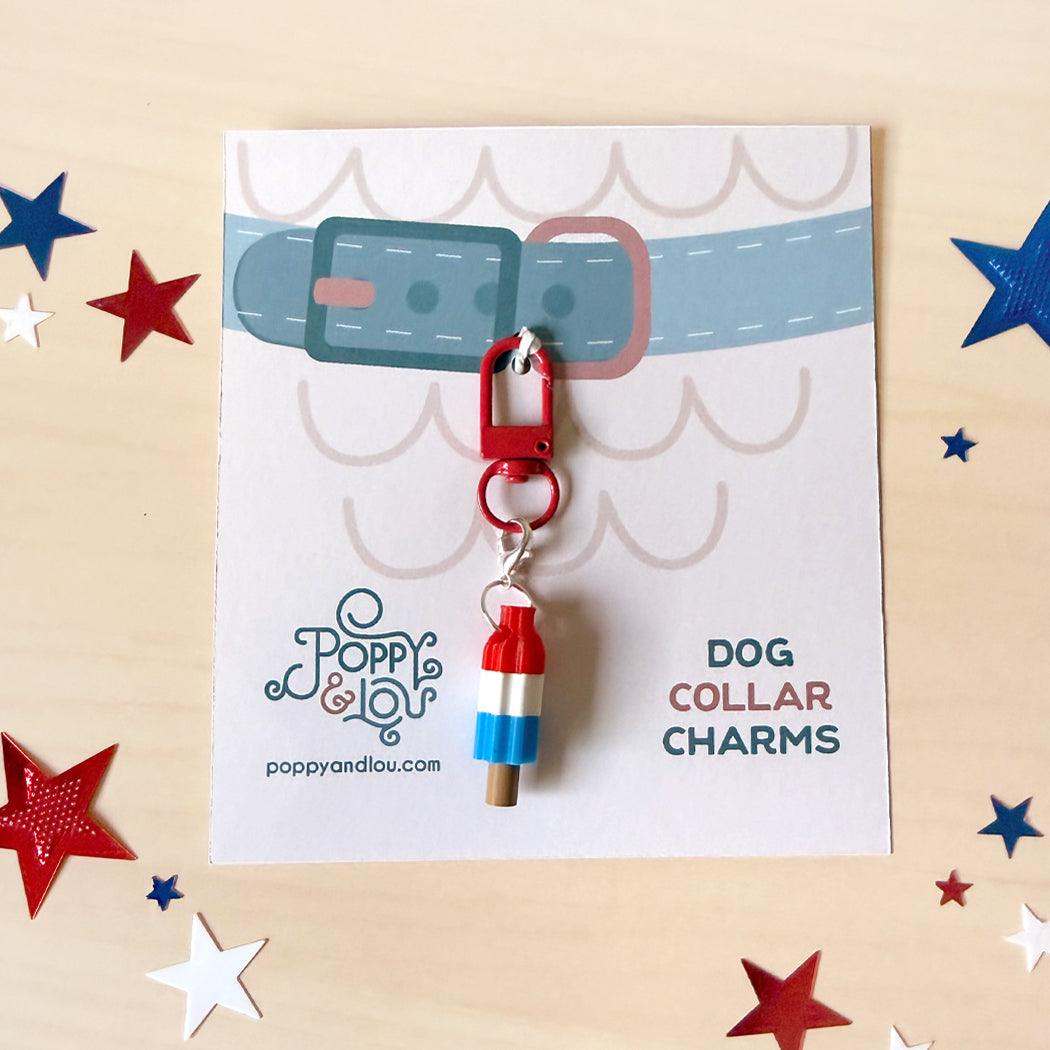 A dog collar charm shaped like a red, white, and blue lighthouse or flag, attached to a red clip and displayed on a branded card. The card reads 'DOG COLLAR CHARMS' and shows the Poppy & Lou brand.