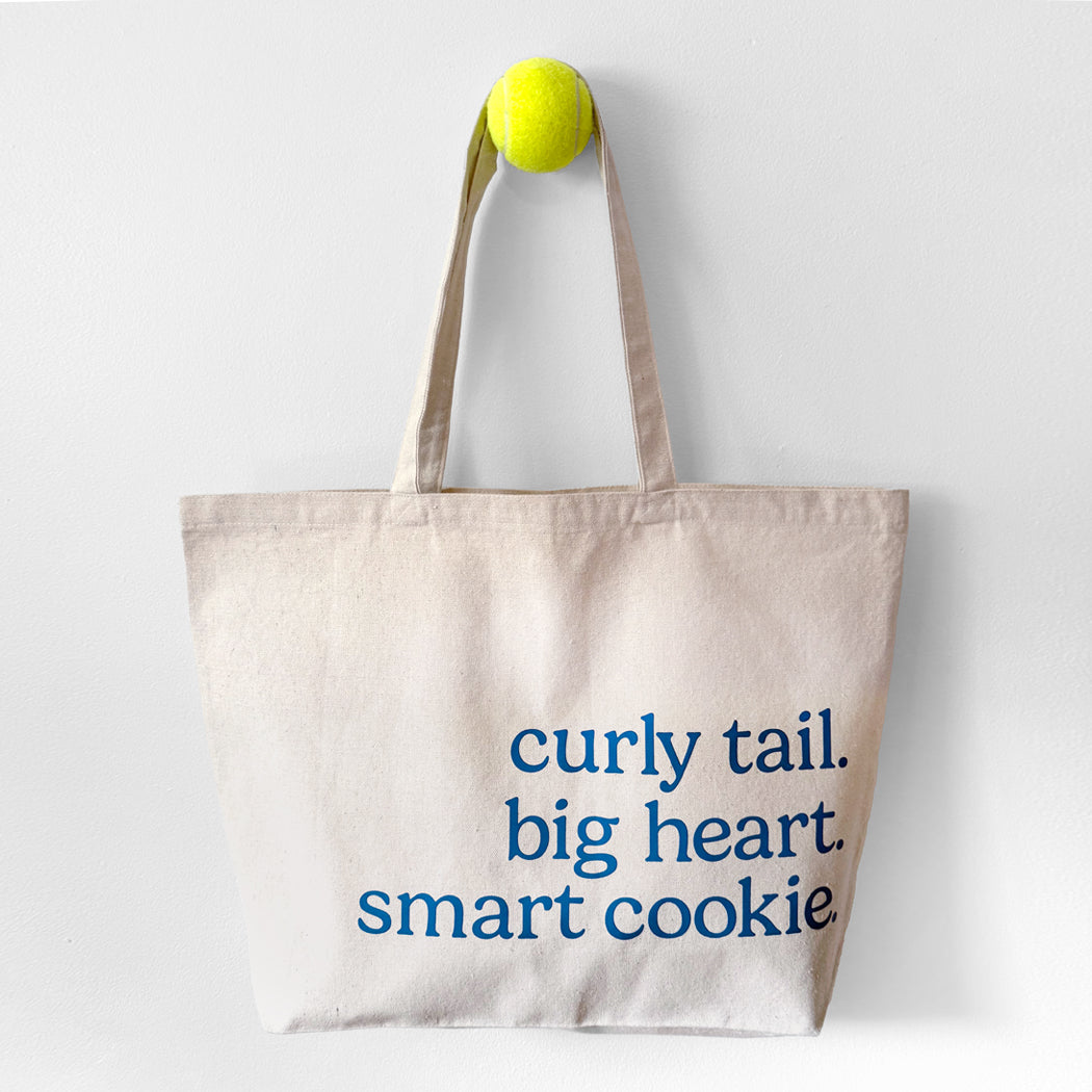 Tote bag with text 'curly tail. big heart. smart cookie' on a white background