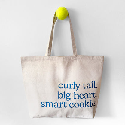 Tote bag with text 'curly tail. big heart. smart cookie' on a white background