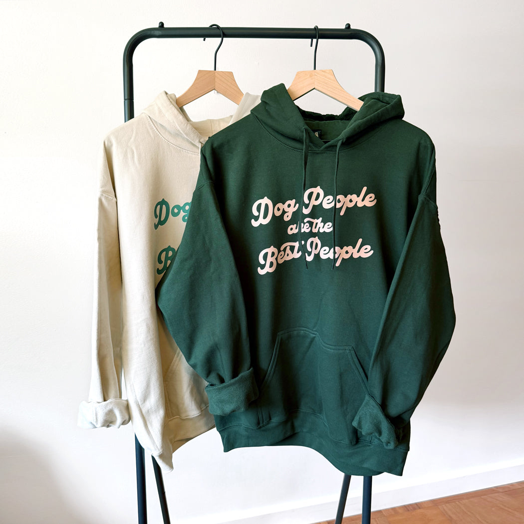 Green hoodie with 'Dog People are the Best People' text on a rack against a white wall.