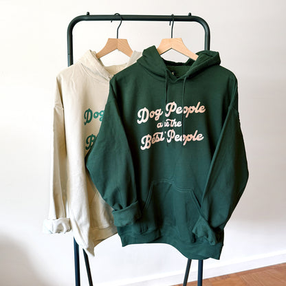 Green hoodie with 'Dog People are the Best People' text on a rack against a white wall.