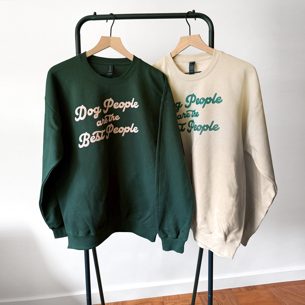 Two sweatshirts on a rack with text design, one green and one beige.