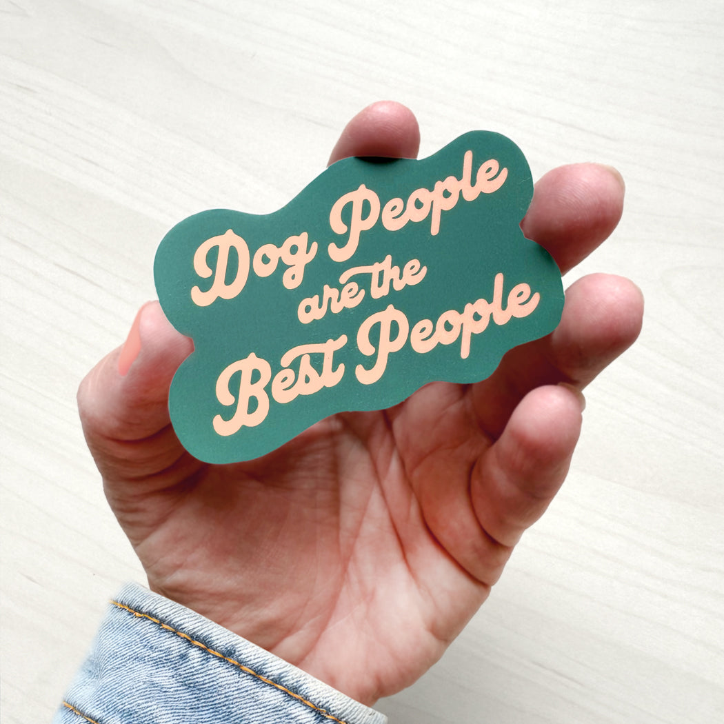 Hand holding a teal and pink 'Dog People are the Best People' sign against a white background