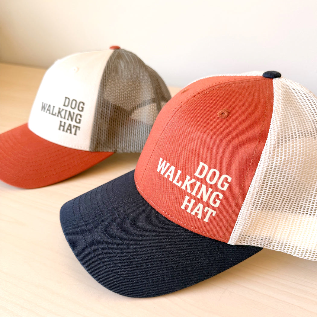 Two 'Dog Walking Hat' caps on a light wooden surface.