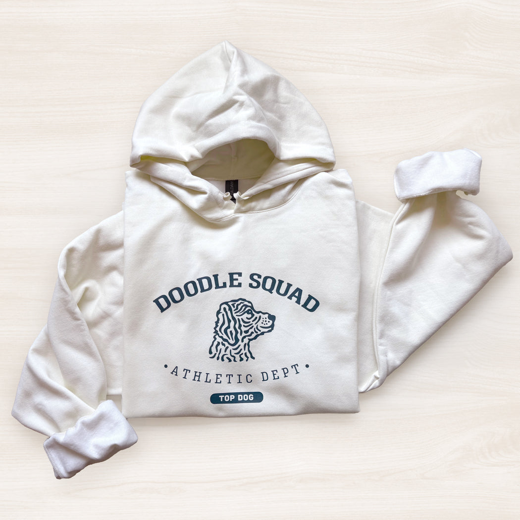 White hoodie with 'Doodle Squad Athletic Dept' text and dog illustration on a light beige background