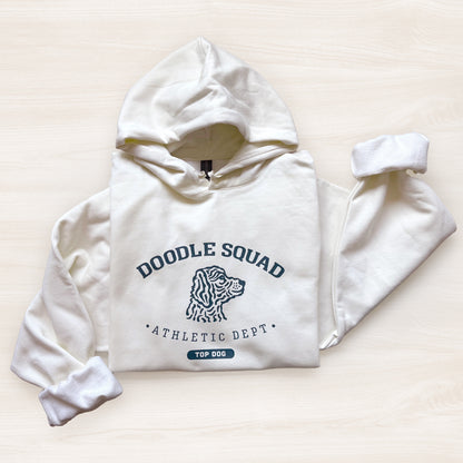 White hoodie with 'Doodle Squad Athletic Dept' text and dog illustration on a light beige background