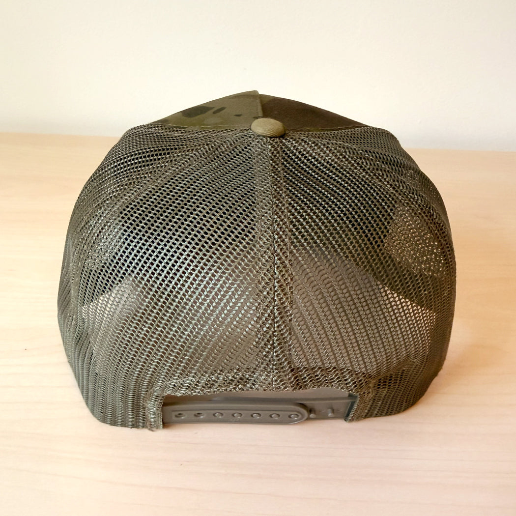 A back view of a dark green camouflage trucker cap with a curved brim and mesh back, featuring the text 'Every Day is a Dog Day' in tan script on the front panel, resting on a light wood surface.