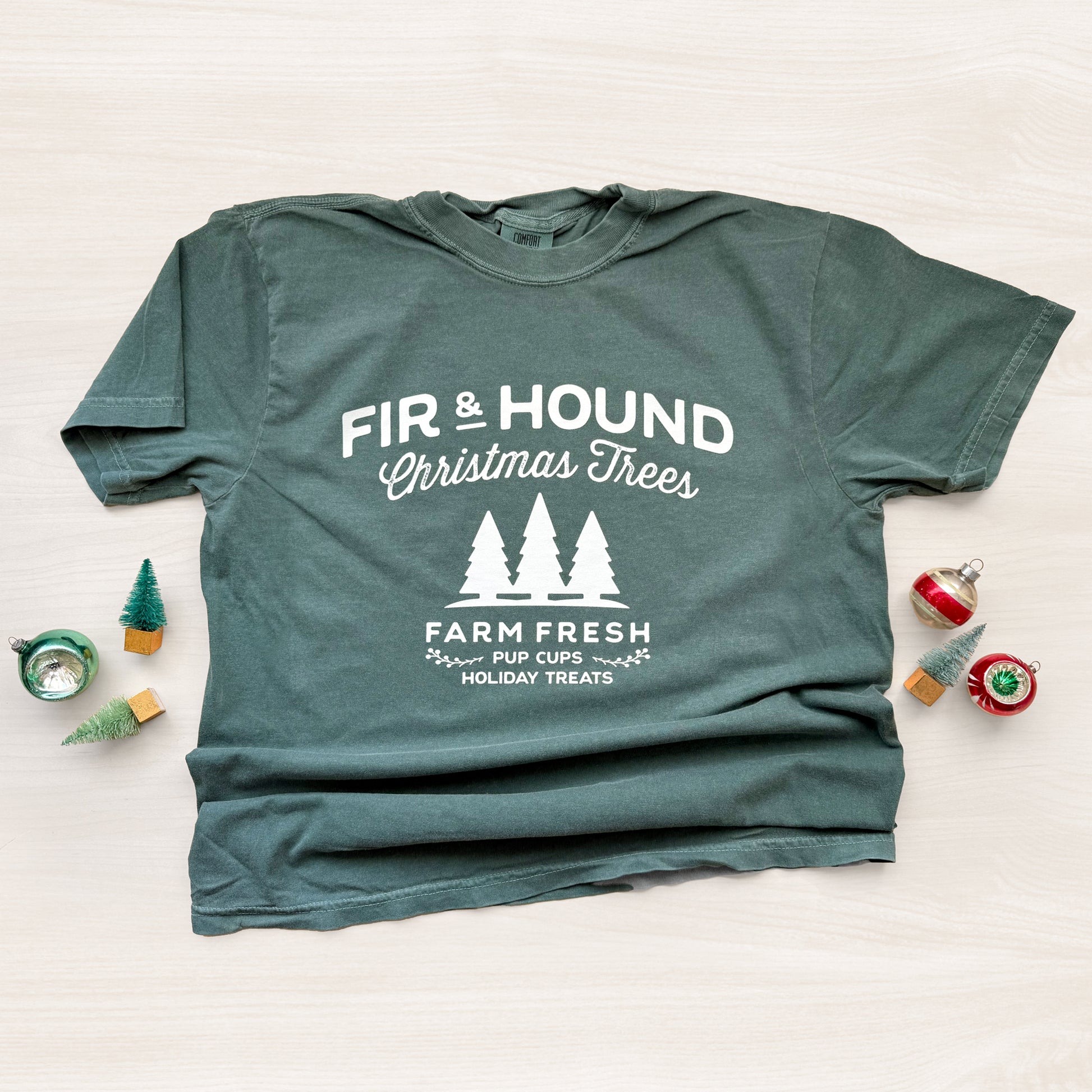 Green t-shirt with 'Fir & Hound Christmas Trees' text and graphics on a light background