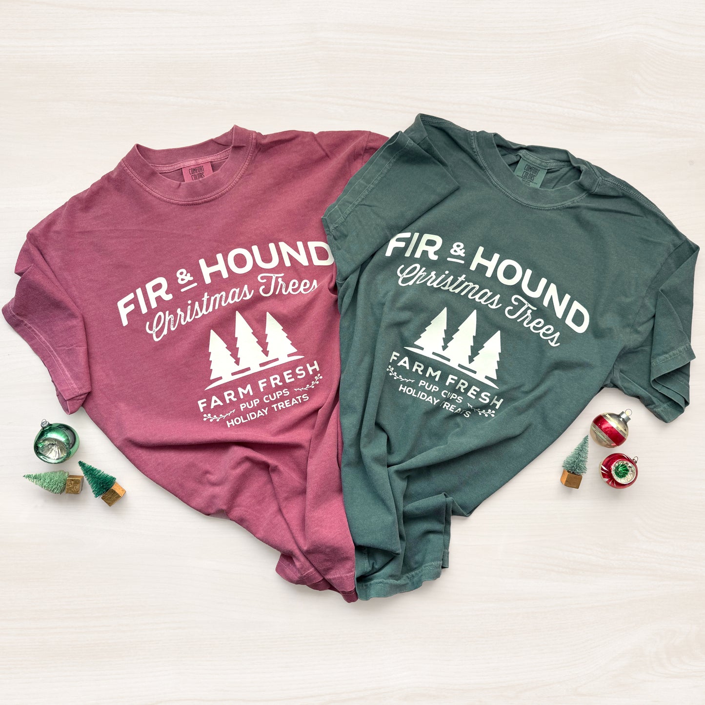 Two t-shirts, one pink and one green, with 'Fir & Hound Christmas Trees' text on a white background.