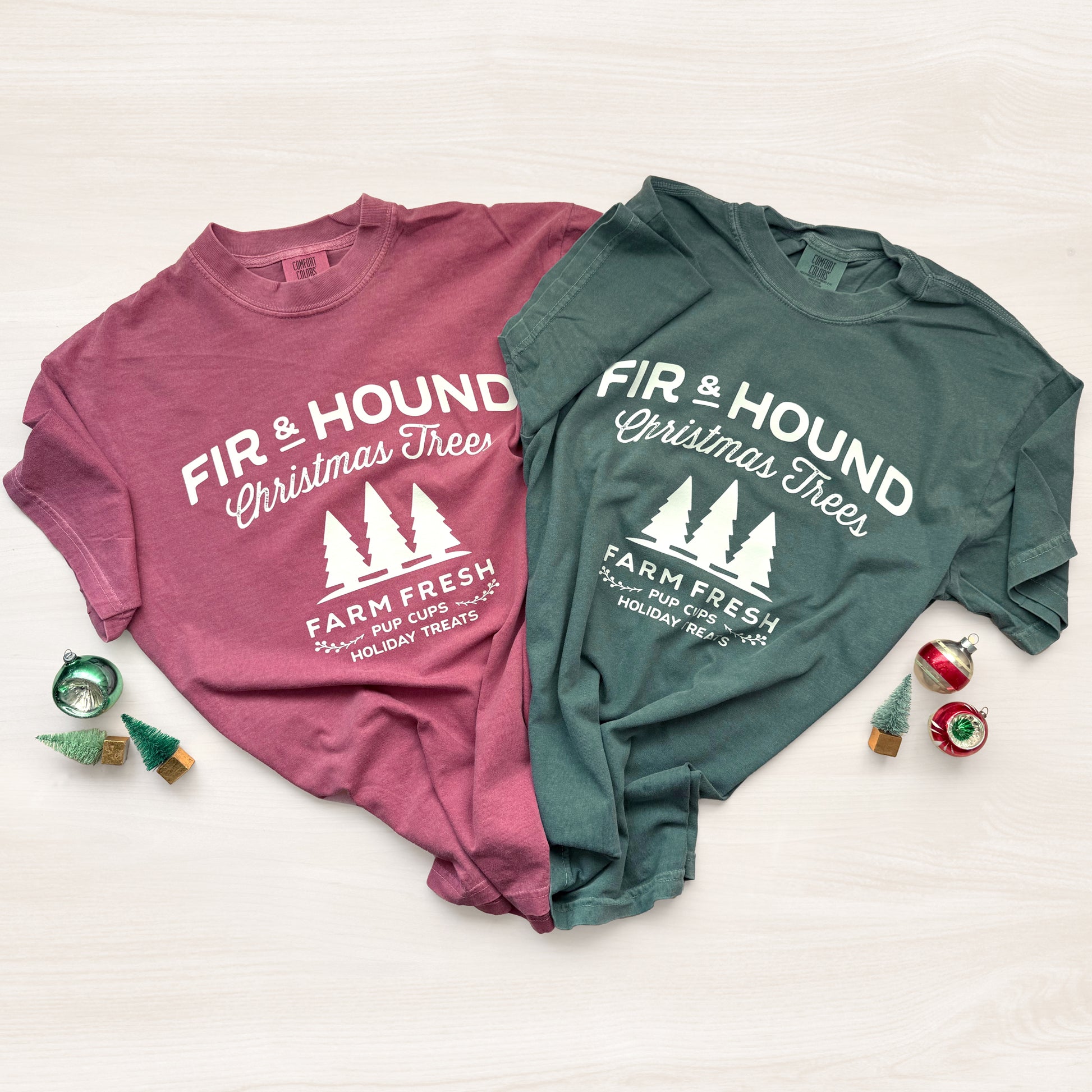 Two t-shirts, one pink and one green, with 'Fir & Hound Christmas Trees' text on a white background.