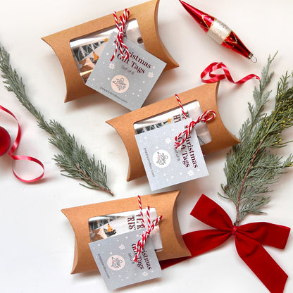 Three brown pillow-shaped gift boxes with red ribbons and Christmas-themed gift tags on a white background.
