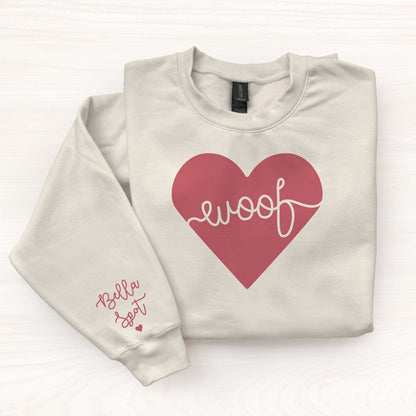 Folded beige sweatshirt with a red heart and 'woof' text on a white background